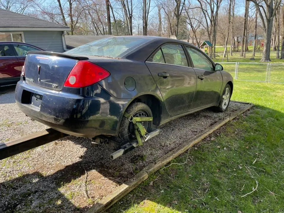 Dark Pontiac G6 sedan parked in a residential driveway, a typical junk car ready to sell in Indianapolis