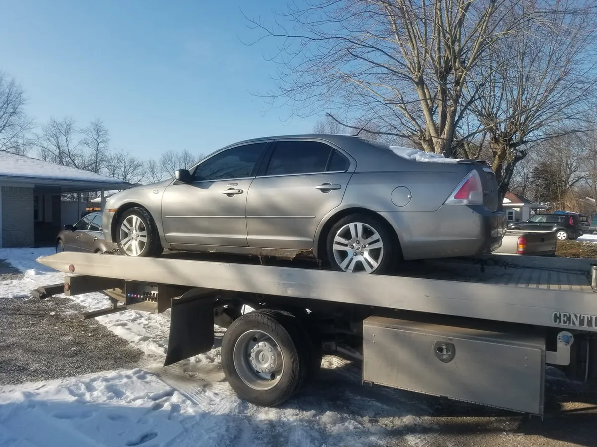 Ford Fusion sedan loaded onto a flatbed tow truck for free pickup by Cash Car Heroes